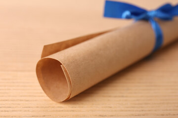 Graduation diploma tied with blue ribbon on wooden table, closeup