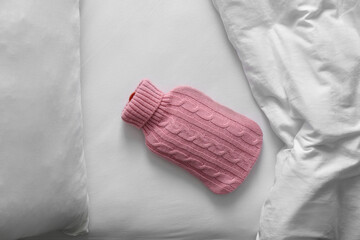 Hot water bottle with knitted cover near soft blanket on bed, top view