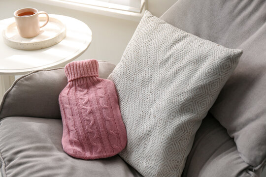 Hot water bottle with knitted cover and cushion on armchair indoors