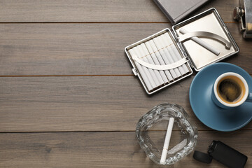 Case with tobacco filter cigarettes, glass ashtray and cup of coffee on wooden table, flat lay....