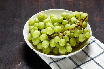 Branch of ripe green grape on plate with water drops. Juicy grapes on wooden background, closeup. Grapes on dark kitchen table with copy space