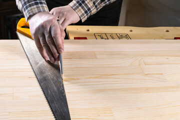 carpenter draws cutting line by pencil on wooden board with hand saw blade on workbench at home