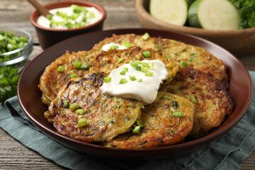 Delicious zucchini pancakes with sour cream served on wooden table, closeup