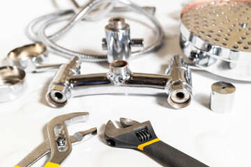 wrenches closeup and disassembled shower faucet on white ceramic shower tray