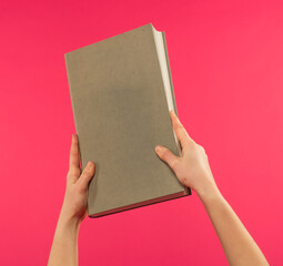 female hands hold a light gray book on a pink background with free space for text