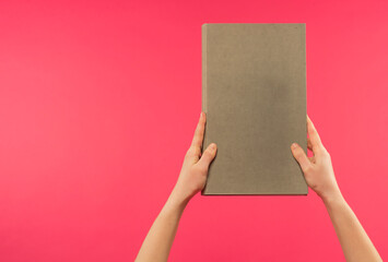 female hands hold a light gray book on a pink background with free space for text