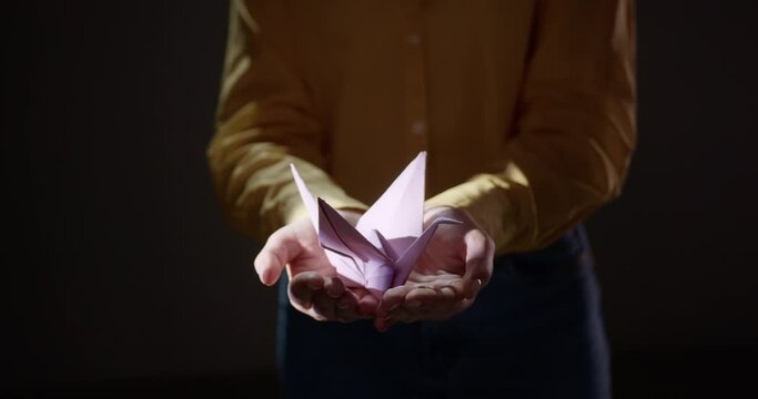 A woman in yellow dress standing in a dark room showing handmade origami bird.