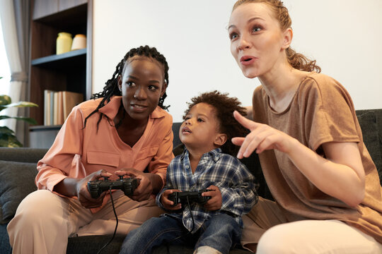 Excited diverse parents and toddler boy playing video game together at home