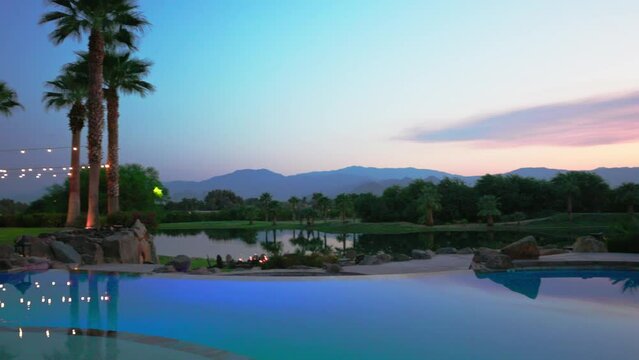 Pool at night time with mountain backdrop palm trees and lights during sunset