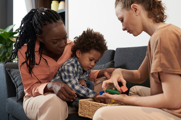 Parents and little son playing with wooden toy blocks at home