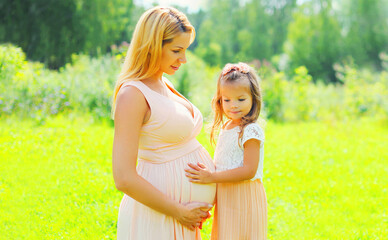 Pregnancy and family concept, happy pregnant woman, little child daughter touches belly mother in summer day