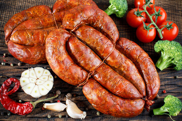 salami sausages from boiled meat on a dark board with pepper, cucumber, tomato, onion and spices. View from above 