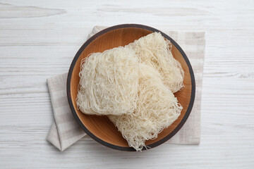 Bowl with dried rice noodles and napkin on white wooden table, top view