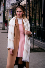 Beautiful girl in striped trench coat and sunglasses with little black cross bag holding coffee to...