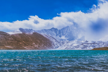 Landscape of a lake with water, sky , mountain, clouds and snow.