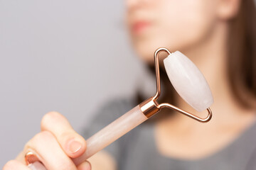 Closeup of a woman using a rose quartz roller to depuff her face in the morning.
