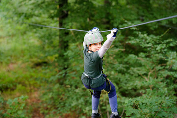 School boy in forest adventure park. Acitve child, kid in helmet climbs on high rope trail. Agility...