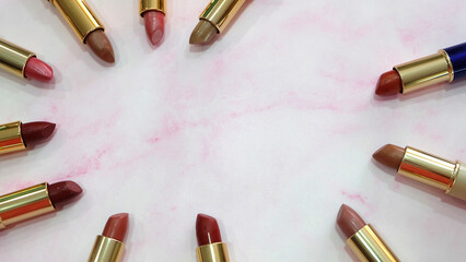 Flat lay of lipsticks in different hues of red arranged in a circle, on a pink marble background. With copy space in the middle.