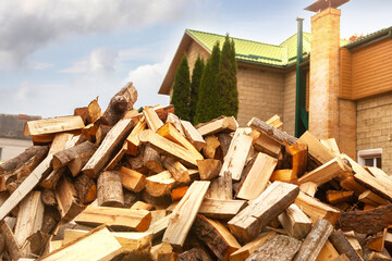 A pile of split firewood for heating the house, unloaded in the yard, against the backdrop of the house, natural heating sources.