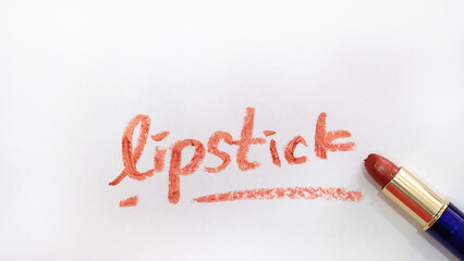 The word 'lipstick' written on a piece of paper with red lipstick, with the lipstick tube placed next to the word.