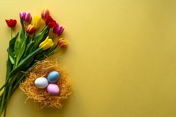 Stylish background with colorful Easter eggs isolated on yellow background with colorful tulip flowers. Flat lay, top view, mockup, overhead, template