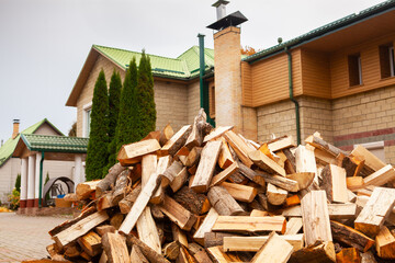 A pile of split firewood for heating the house, unloaded in the yard, against the backdrop of the house, natural heating sources.