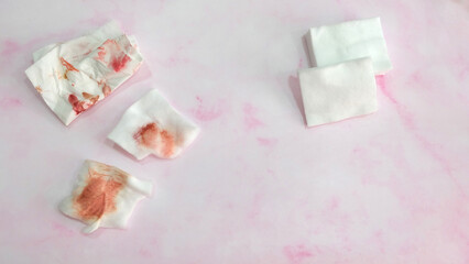 Pieces of cotton pads and tissue paper with red stain from wiping off make-up. With clean cotton pad on the right.