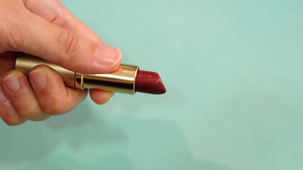 Hand holding a tube of dark red lipstick, with the lip off.