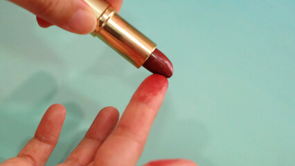 Hand holding a tube of red lipstick, with the tip smudging the tip of a finger.