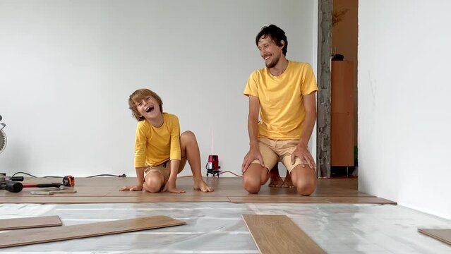 Father and his little son install laminate on the floor in their apartment. DIY concept. Slowmotion video