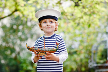 Happy little kid boy in sailor capitain hat and uniform playing with sailor boat ship. Smiling...