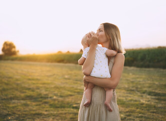 Fototapeta na wymiar Loving mother and baby at sunset. Beautiful woman and small child in nature background. Concept of natural motherhood. Happy healthy family at summer outdoors. Positive human emotions and feelings.
