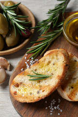 Tasty bruschettas with oil and rosemary on wooden board, closeup