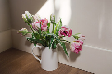 Pink tulip flower bouquet with green fresh stems in a white porcelain jar vase on a white window frame background. Vibrant colourful botany floral home decor idea.