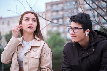 A couple of latin teenagers sharing earphones to listen to music outdoors.