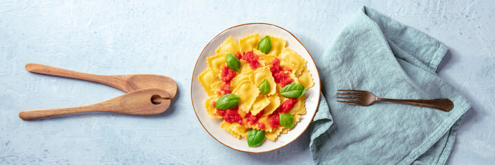 Italian ravioli with red tomato sauce and basil, overhead flat lay panorama with a fork and wooden spoons