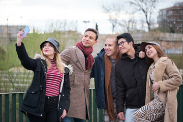 Group of friends of different ages and ethnicities taking a selfie outdoors in winter.