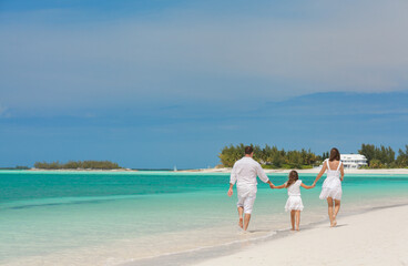 Happy family with daughter walking aquamarine shallows barefoot