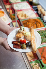 hand holding a plate with vegetables, meat and a bread stick 