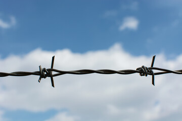 Barbed wire with blue sky with background clouds, with space for your text.