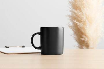 Obraz na płótnie Canvas Black mug mockup with a clipboard on the wooden table with a pampas decoration.
