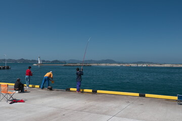 岸壁で魚を釣る人たちと青空と青い海
