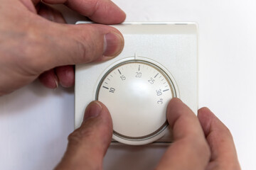 A person turning down the central heating room thermostat to save on energy cost.