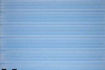 Blaues Rolltor und Industrietor einer großen Lagerhalle vor blauem Himmel im Sonnenschein in...