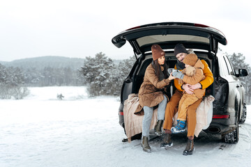 Winter portrait of a family sit on car trunk enjoy their vacation in forest