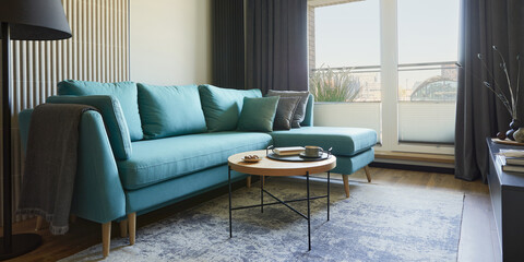 Creative composition of modern living room interior in small apartment. Eucalyptus sofa, coffee table and personal accessories. Windows with a big city view on. Template.