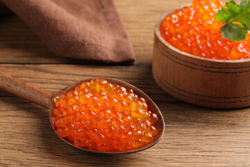 Spoon and bowl with delicious red caviar on wooden table, closeup