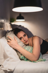 Chica joven delgada tumbada de lado sobre cama de hotel mientras descansa y mira el smartphone