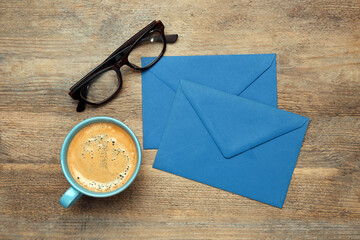 Blue envelopes, cup of coffee and glasses on wooden table, flat lay