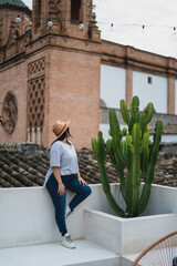Chica guapa joven apoyada en pared blanca con iglesia de fondo en azotea de un hotel estilo soho